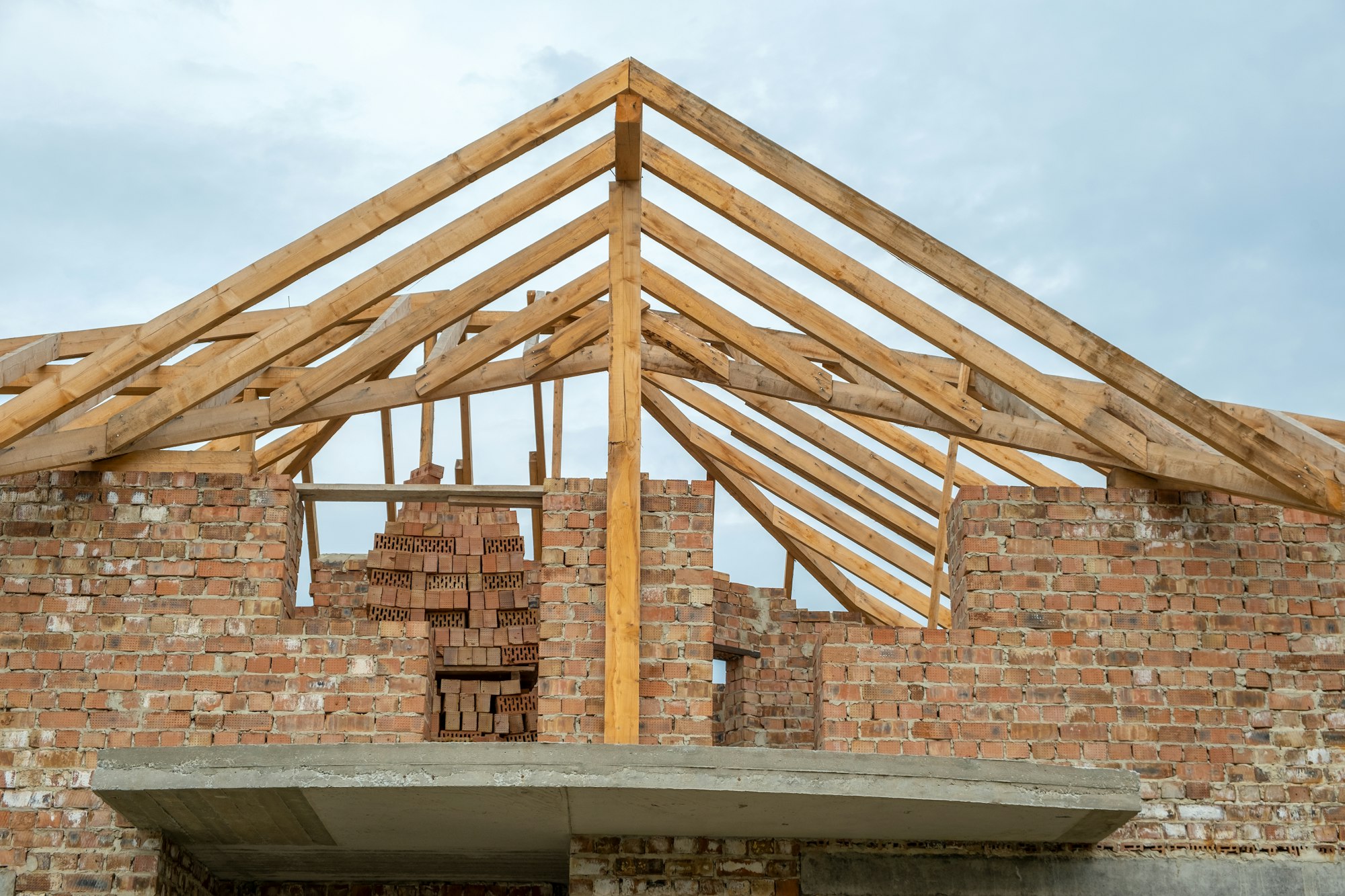 Building site with unfinished brick house with wooden roofing frame for future roof under